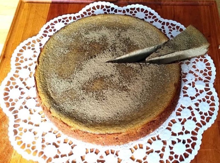 Hojicha Cheesecake auf weißem Spitzendeckchen auf einem Holzbrett, ein Stück ist angeschnitten