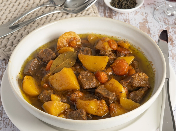 rinderschmortopf mit kartoffeln und grüntee rinderschmortopf mit kartoffeln, möhren und lorbeerblatt in einem weißen Suppenteller